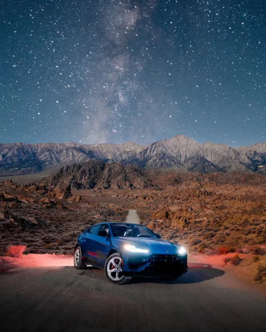 Blue sports car with headlights on in the desert beneath the Milky Way