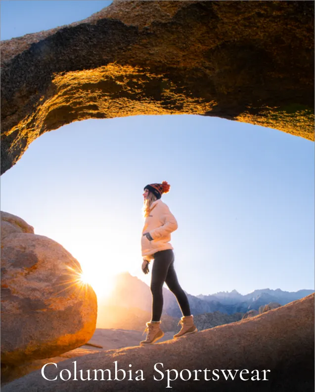 Columbia Sportswear: Hiker in a red beanie beneath a rock arch with a sunburst