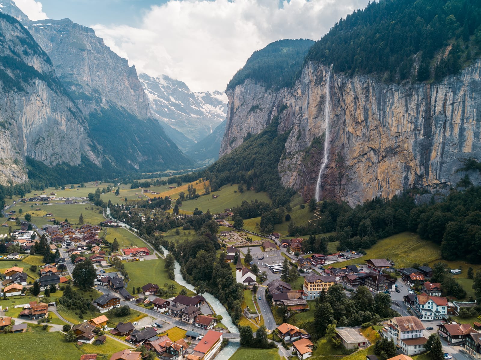 Aerial view of the Lauterbrunnen valley village beneath sheer cliffs and a tall waterfall.